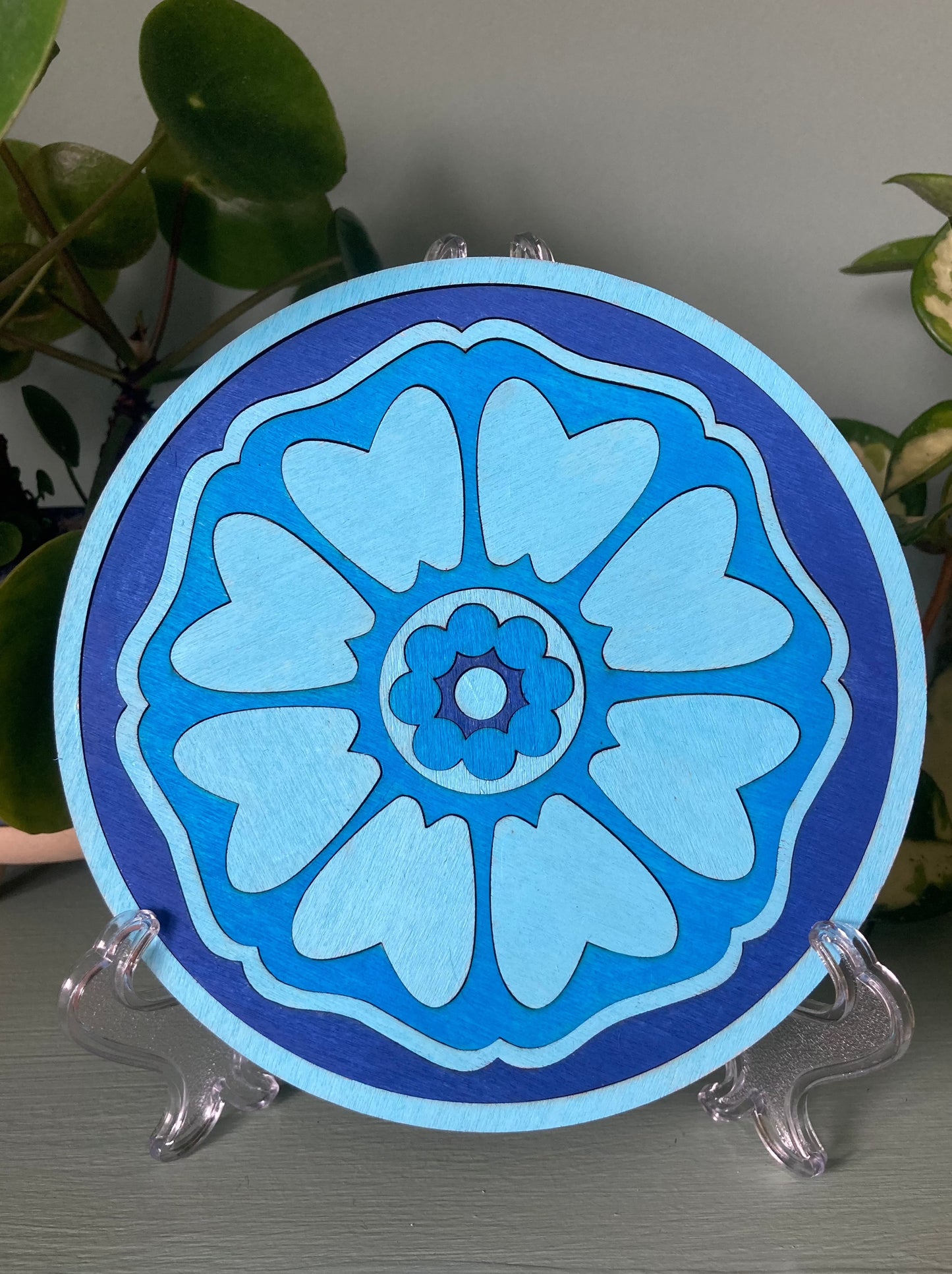 Lotus patterned wooden tile resting on a plastic kickstand. Colour blue.